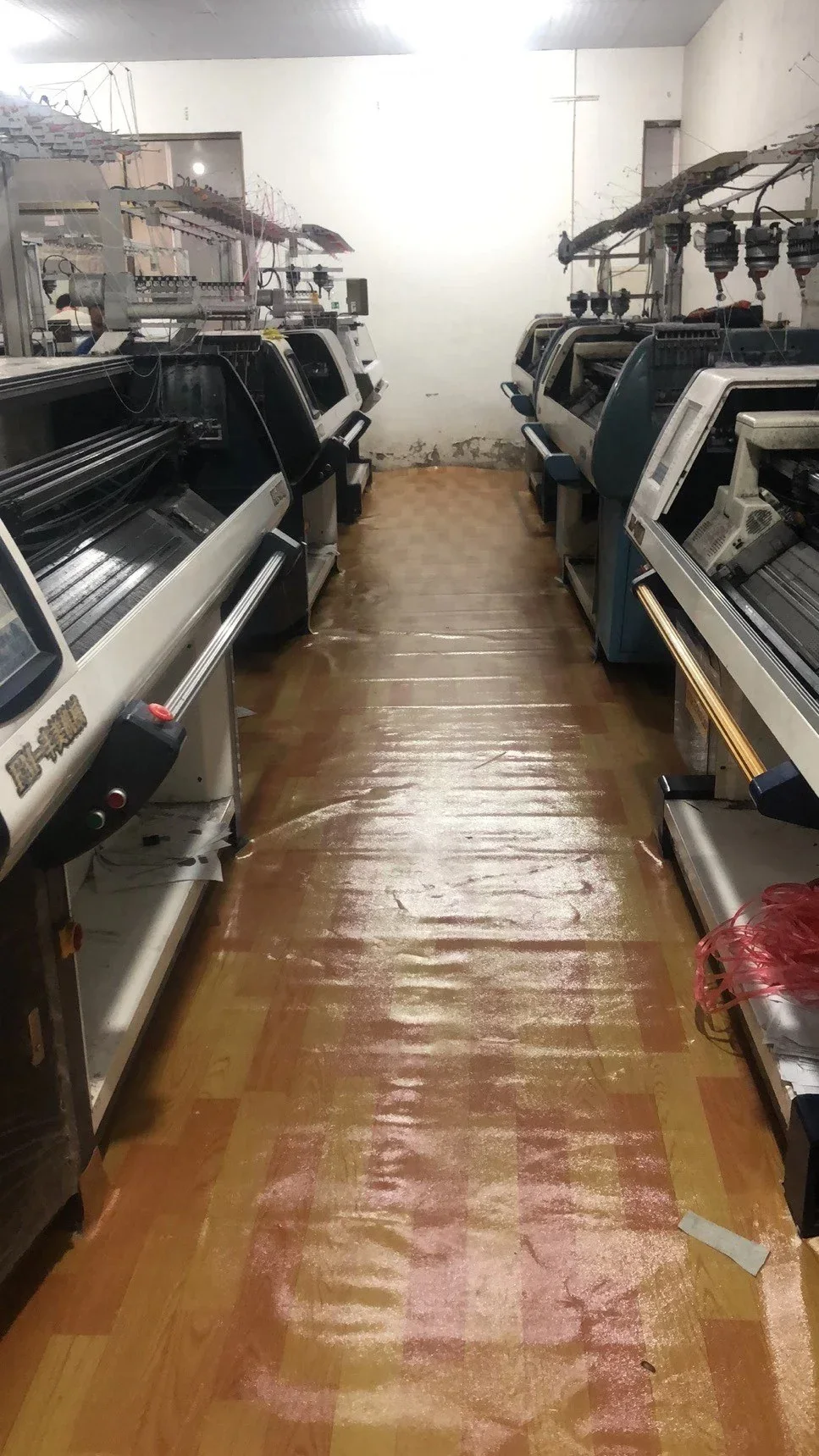 Aisle between flat bed knitting machines on a tiled workshop floor