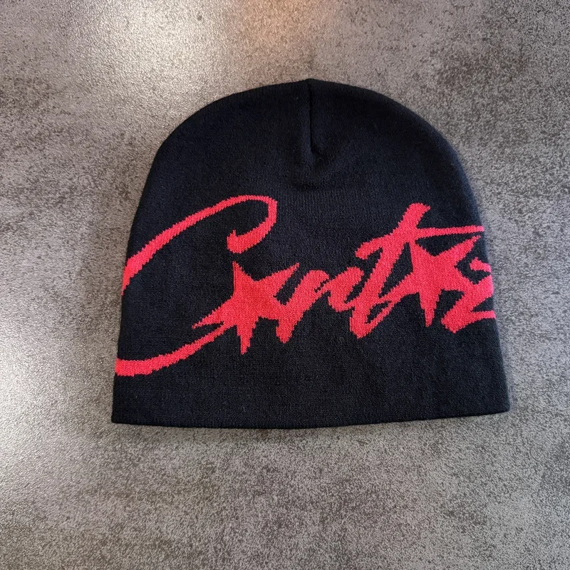 Black knit beanie with a red graphic motif photographed on a grey textured surface.