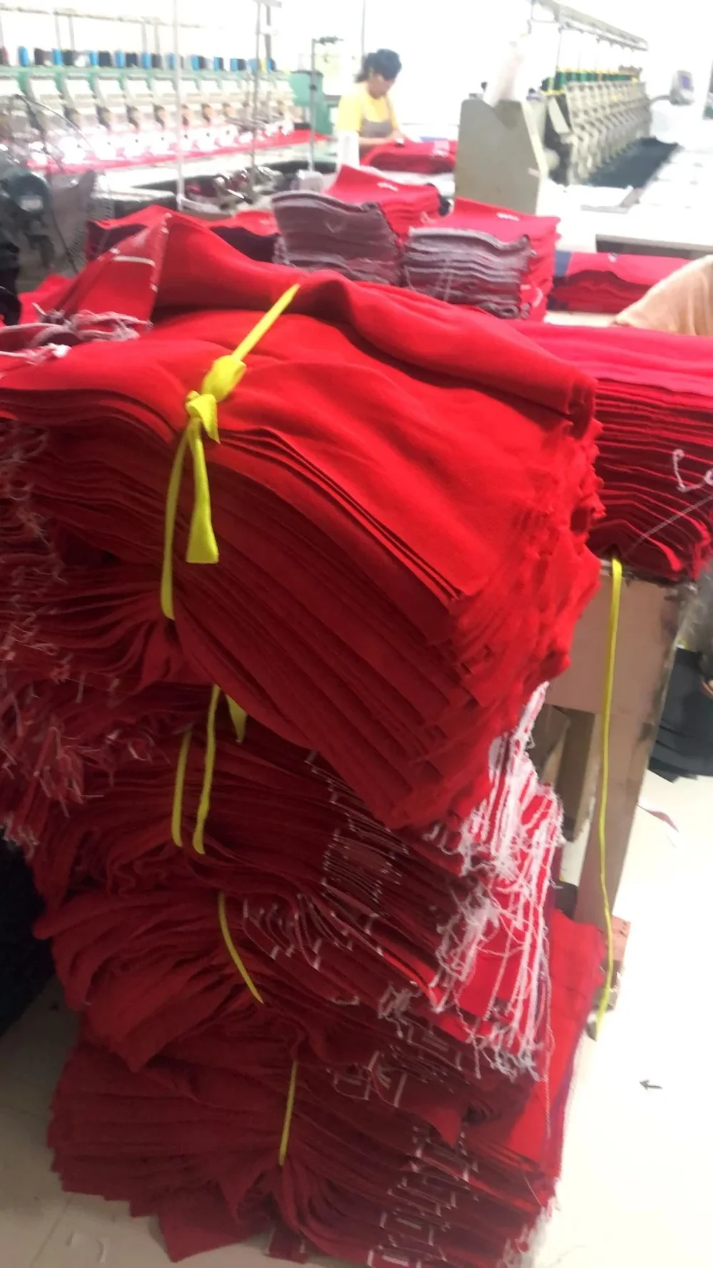 Bundles of red textile panels stacked beside an embroidery machine