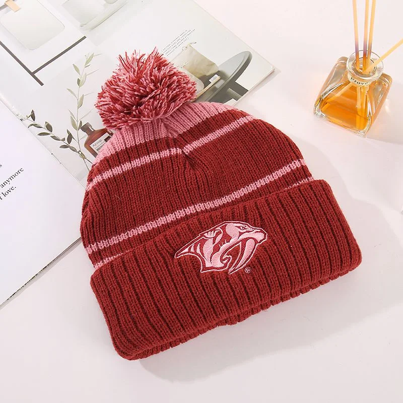 Burgundy striped pom pom beanie with an embroidered front emblem angled view