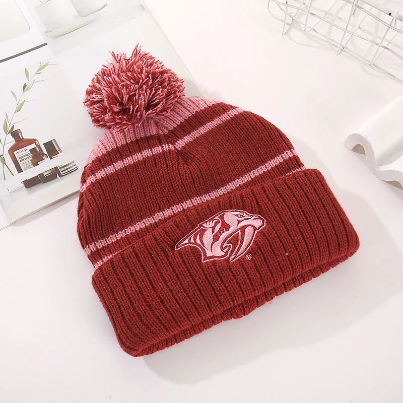 Burgundy striped pom pom beanie with an embroidered sports style emblem